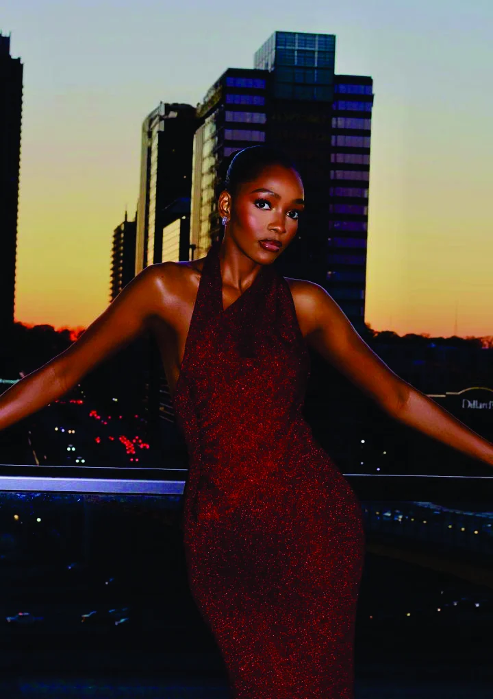Chioma Obiadi in a red sparkle halter gown against a sunset city skyline