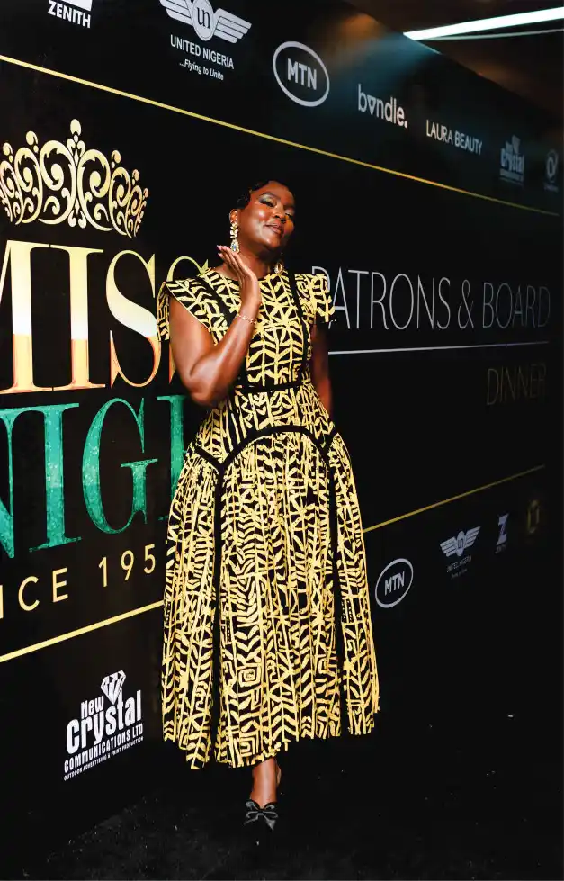 Woman in yellow/gold by Miss Nigeria signage