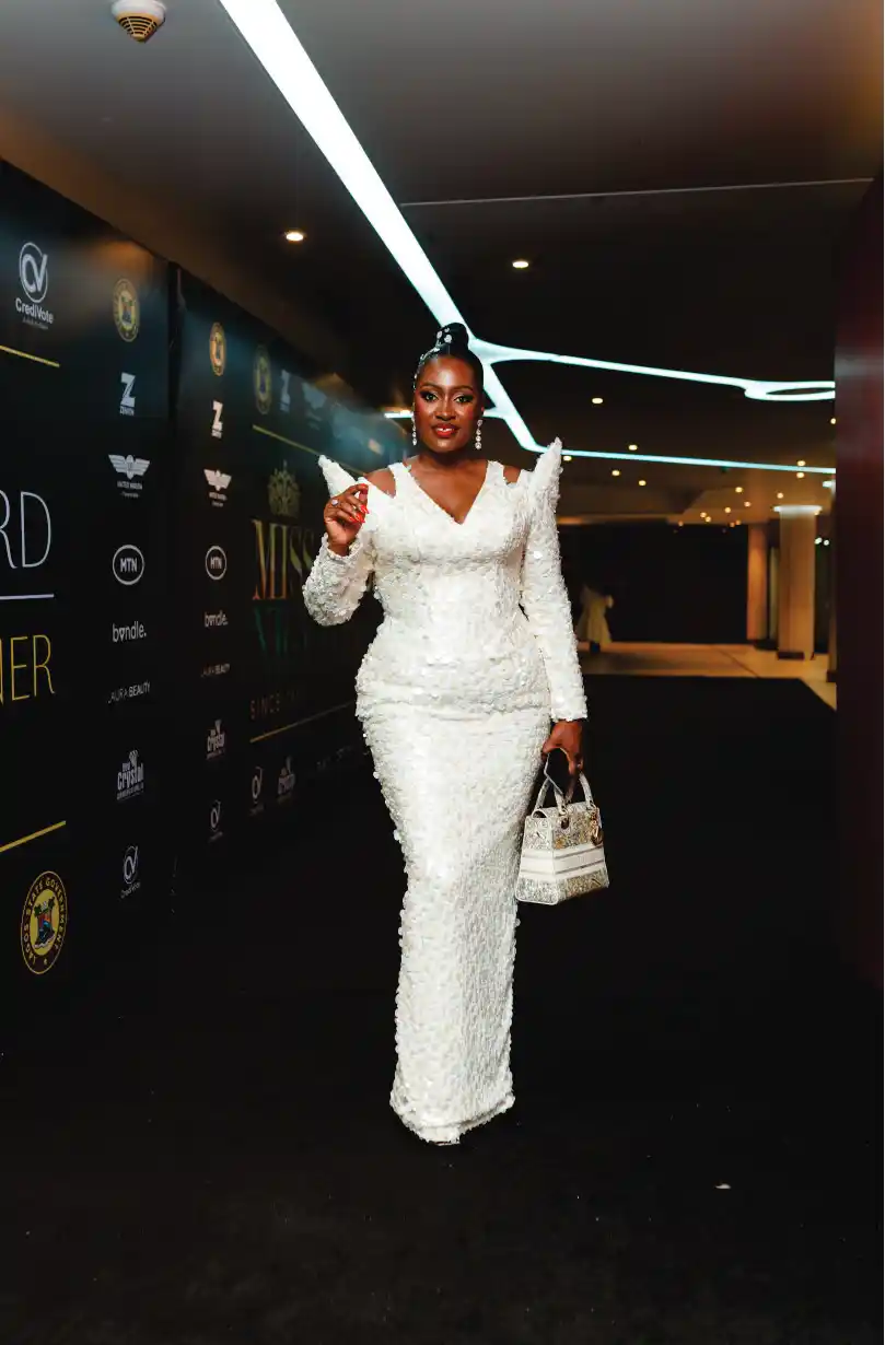 Woman in colorful gown by Miss Nigeria banner