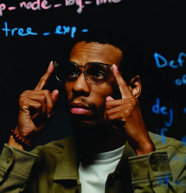 A man in glasses with fingers pressed to his temples against a backdrop of code