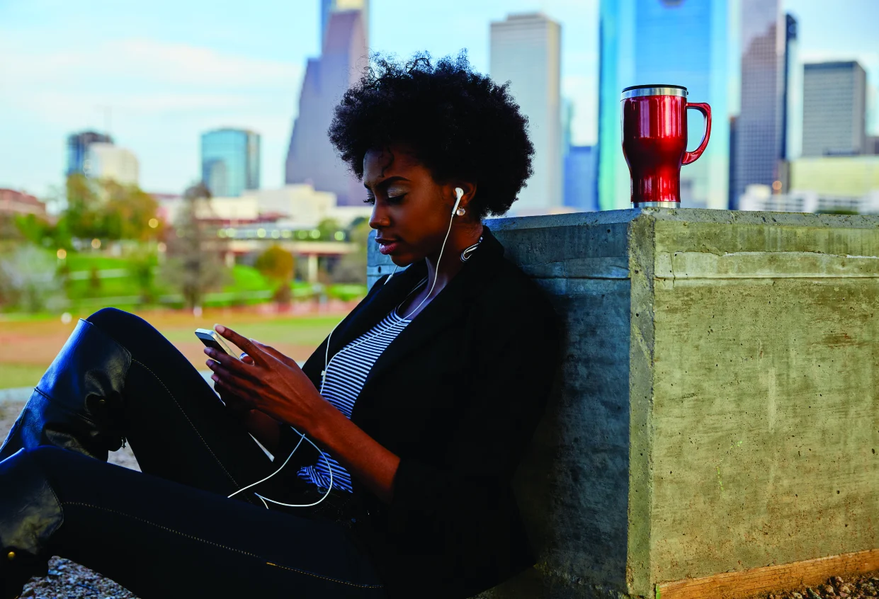 A woman scrolling her phone while leaning on a wall, city skyline behind her