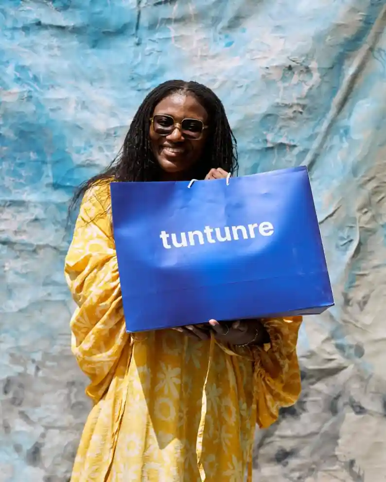 Woman in yellow coat holding a blue Tuntunre shopping bag
