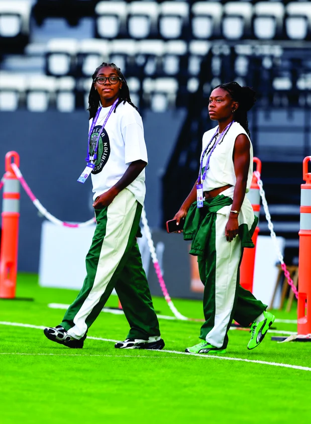 Two Super Falcons walking pitch-side in green and white tracksuits