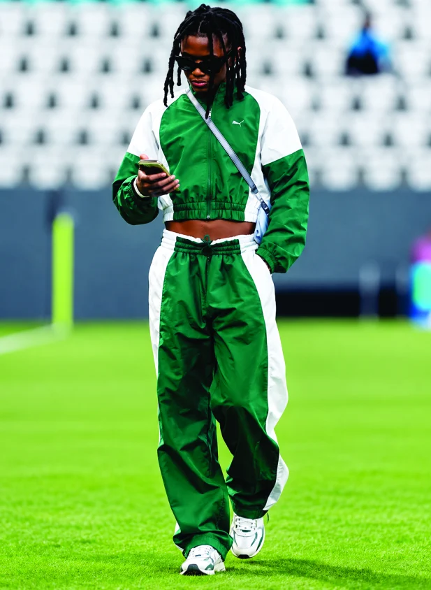 A Super Falcon in a green crop jacket checking her phone on the pitch
